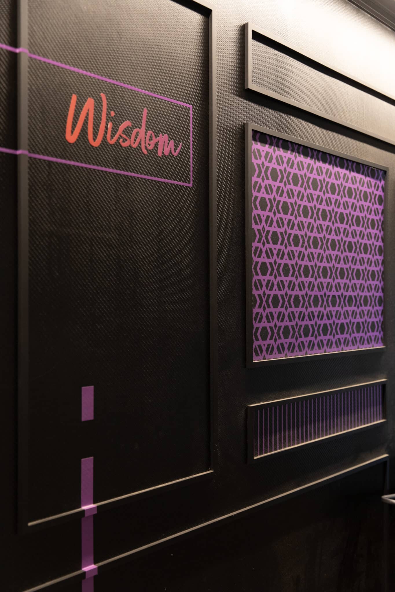 Wisdom neon script on a dark panelled wall with a lit pattern