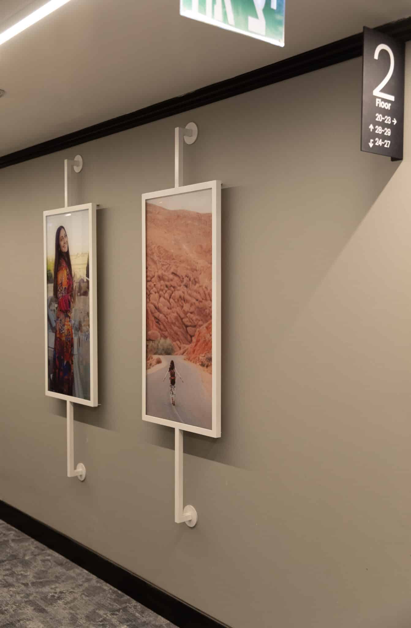 Framed photographs on suspension rods beside floor directory signage