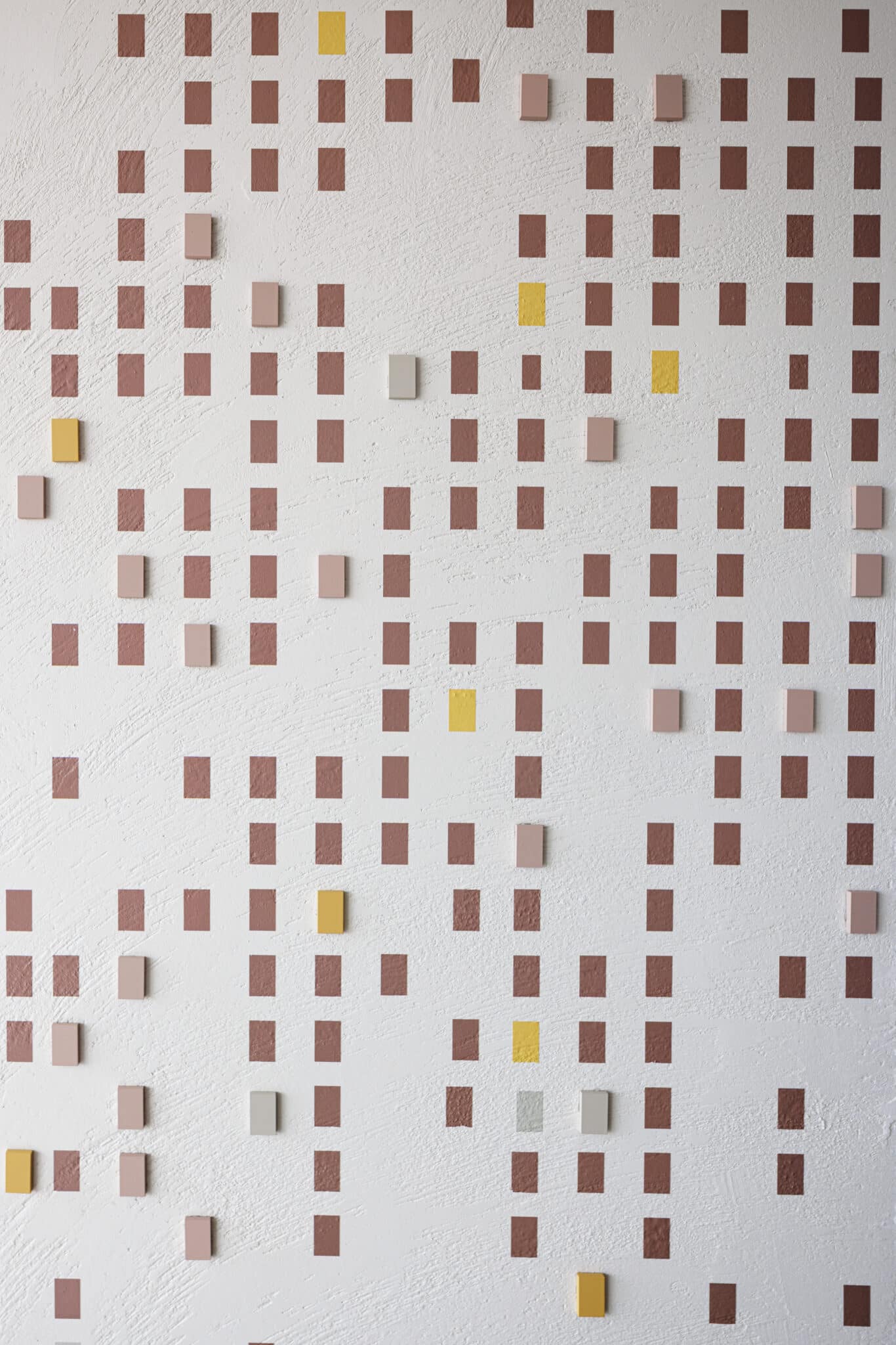Grid of small 3D tiles in muted pink and yellow on a wall