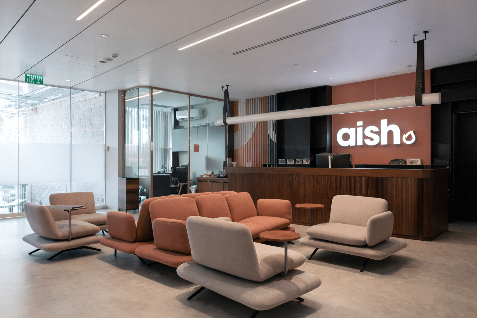 aish lobby with lounge chairs and lit logo above the desk
