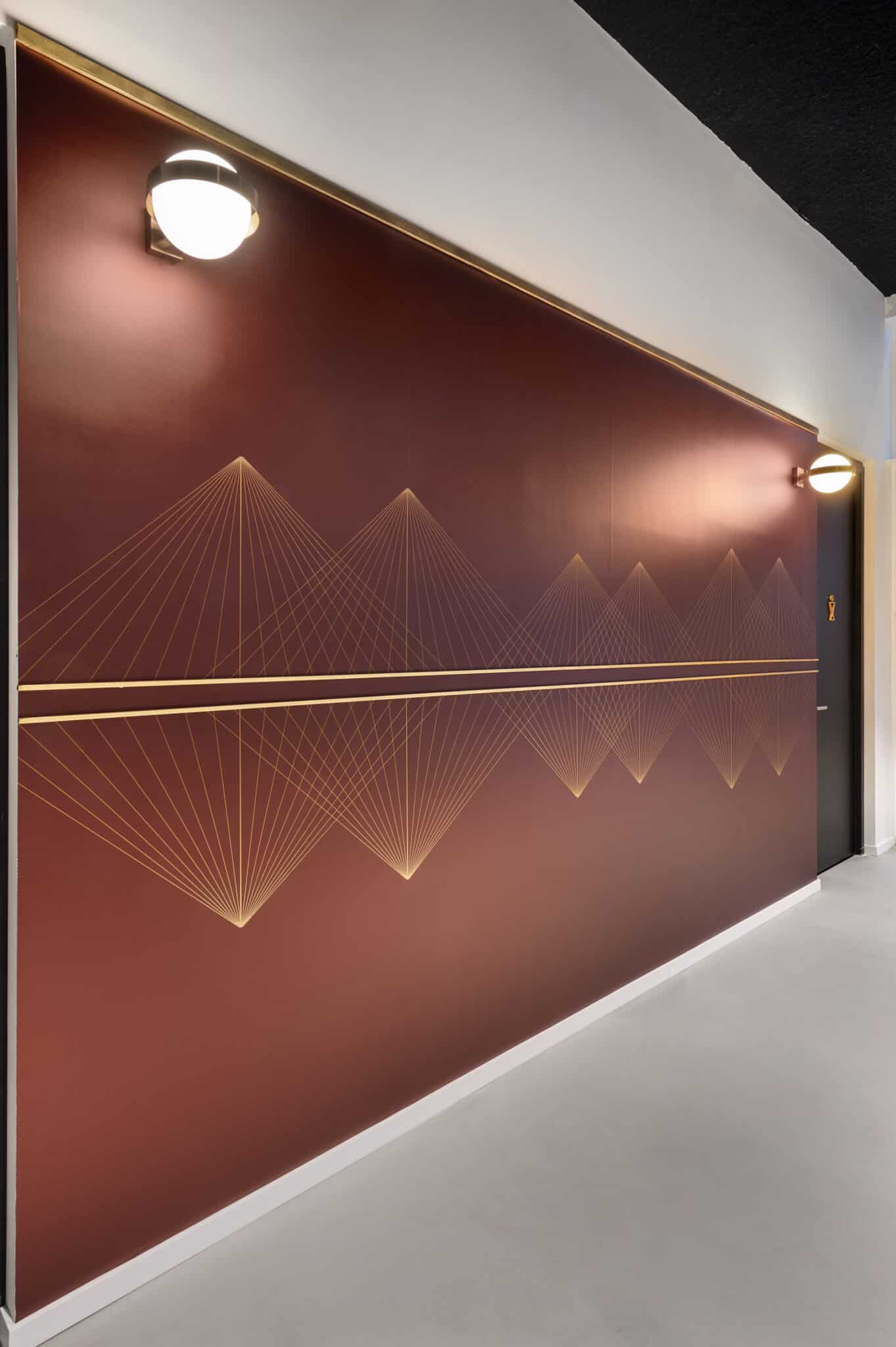 Gold line graphic in a triangular pattern on a burgundy corridor wall