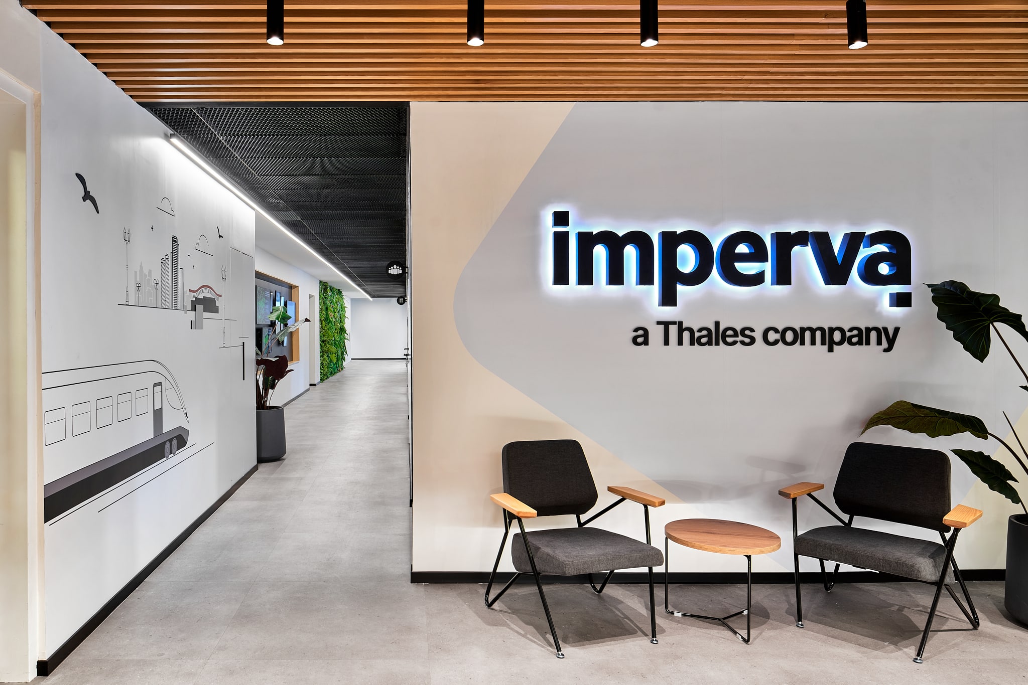 Backlit imperva logo on a curved wall beside a train line drawing