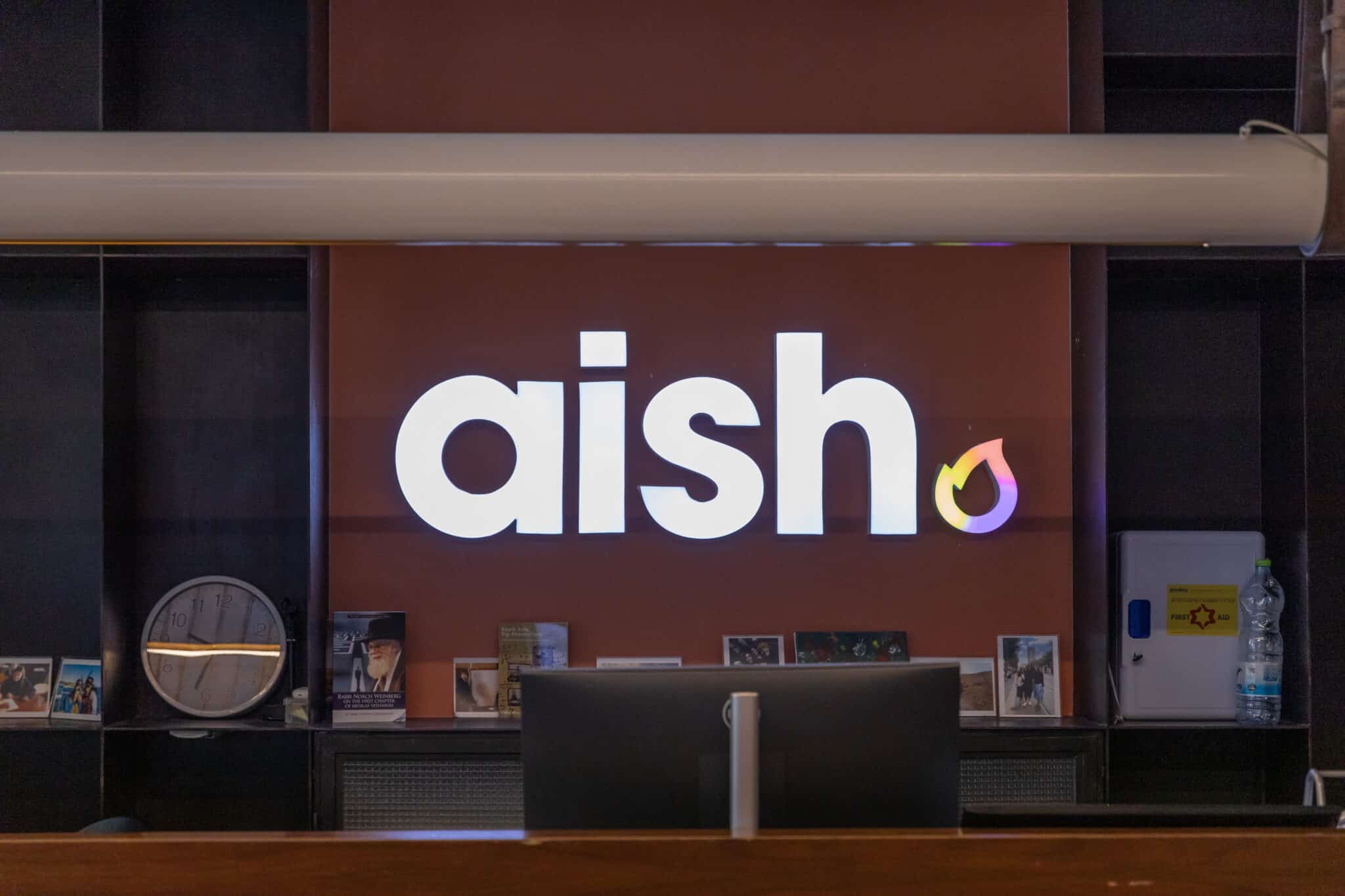 Backlit aish logo above a reception counter