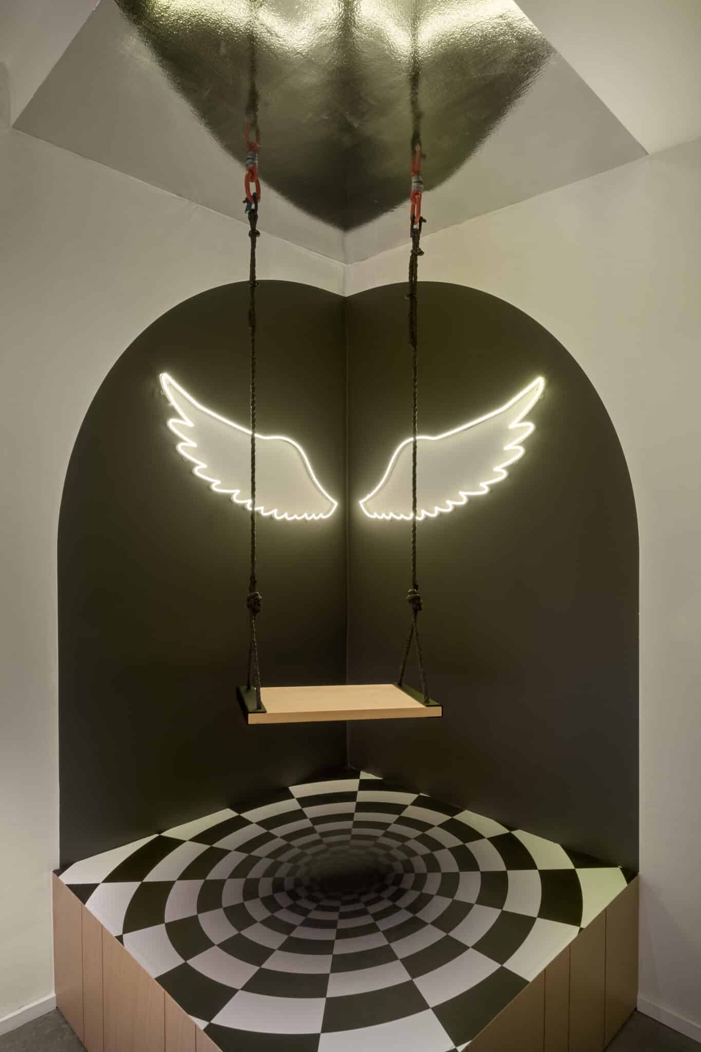Neon angel wings above a swing seat in a dark alcove