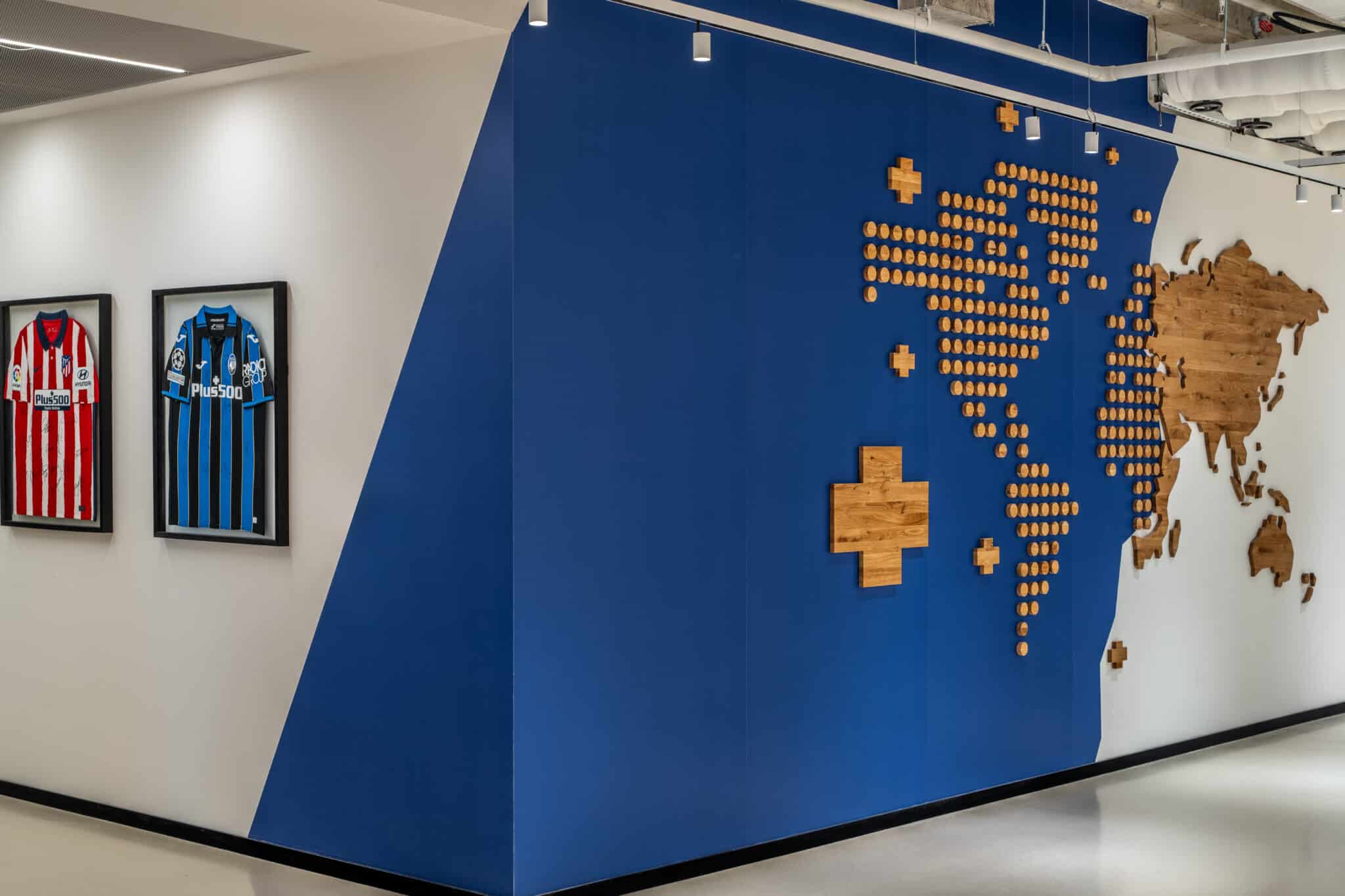 Wood cross world map on a blue wall beside framed football shirts