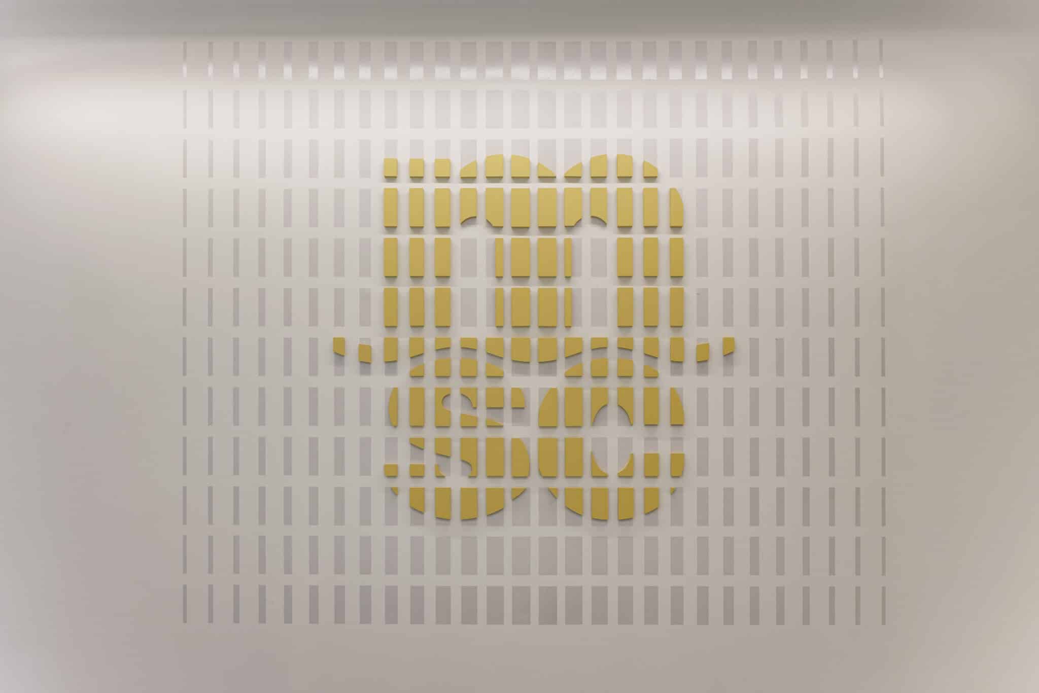 Yellow logo cut into a slatted white wall panel