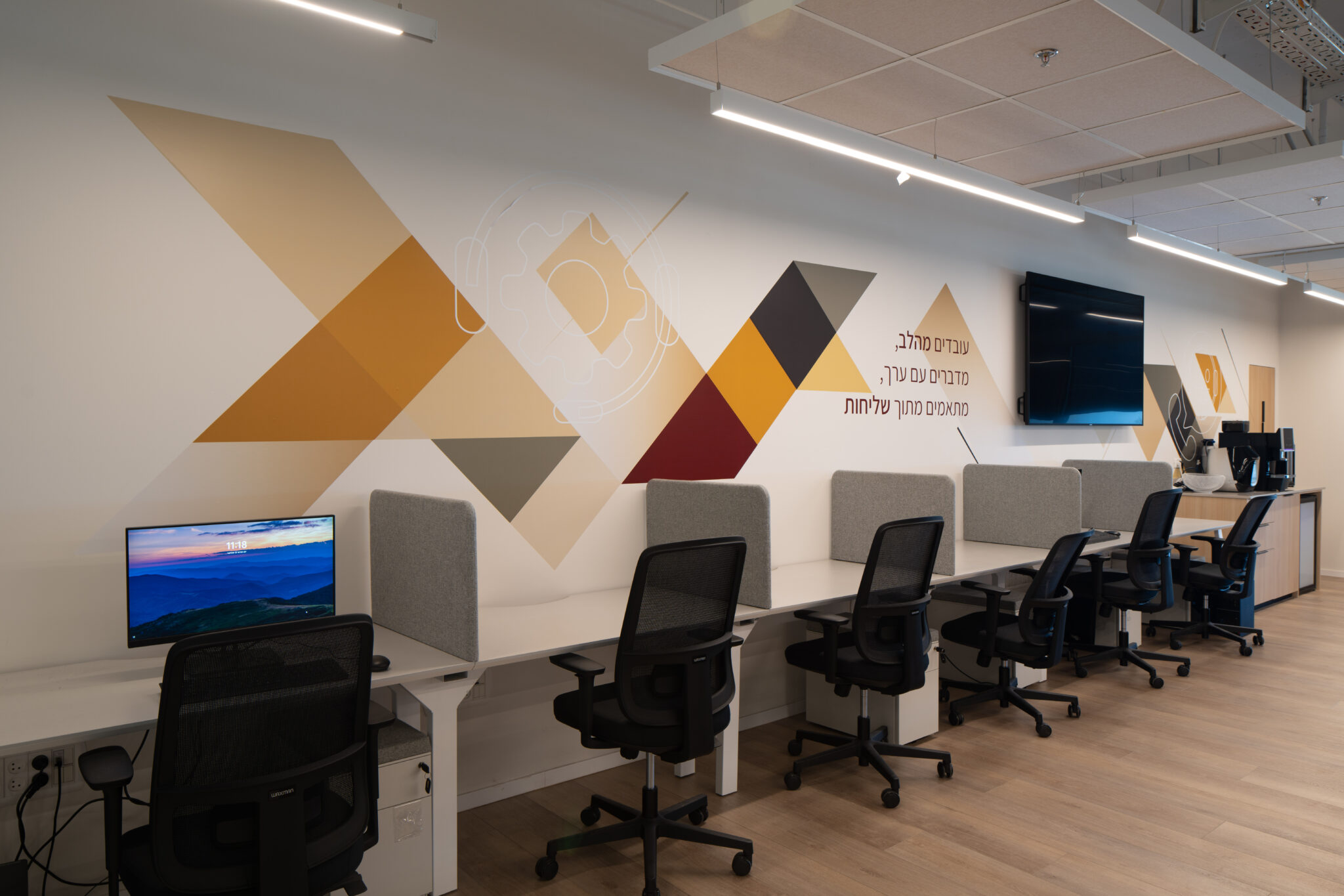 Workstations below a large geometric wall graphic with Hebrew text
