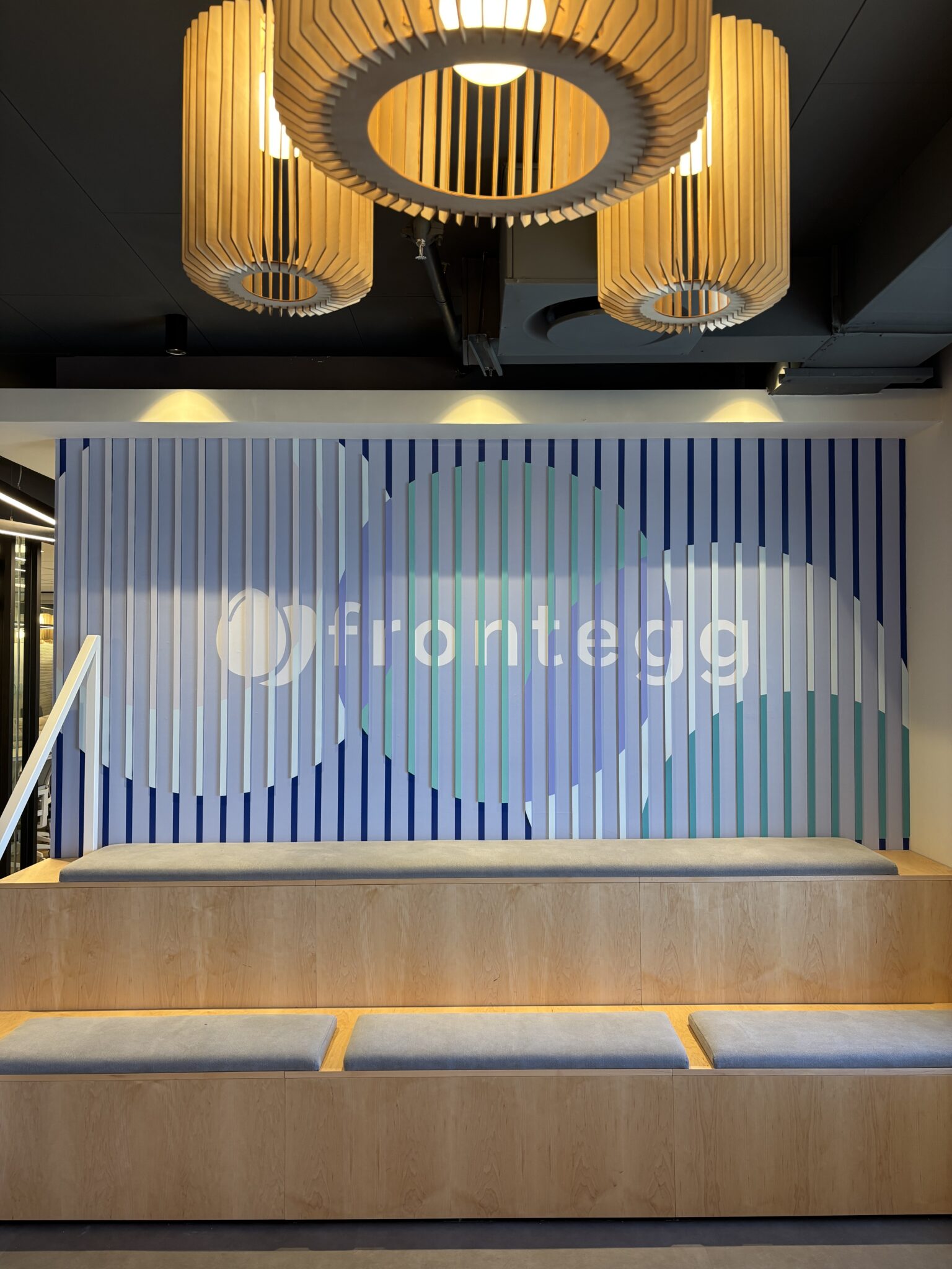 frontegg logo on a blue slat wall above wooden seating