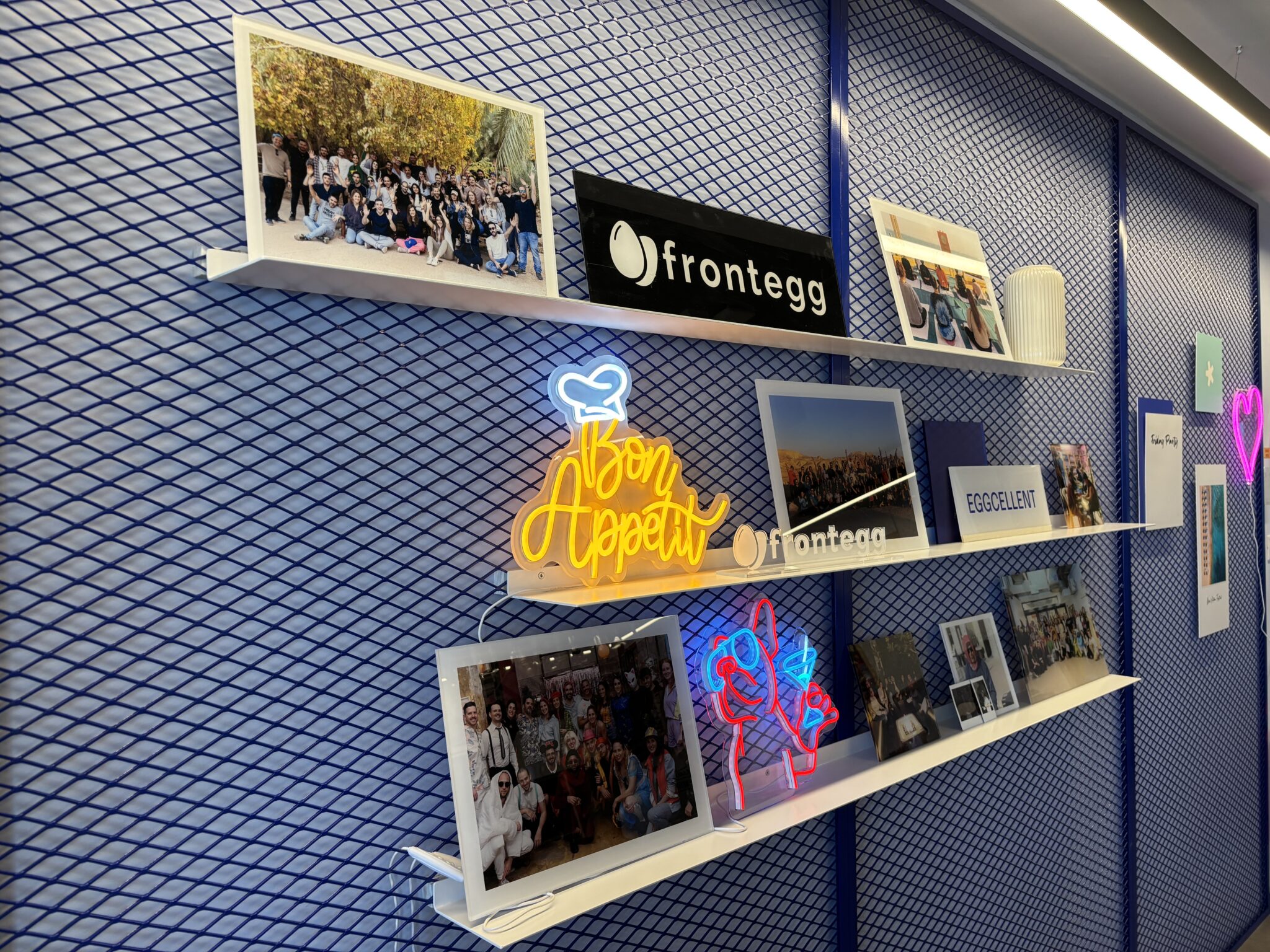 frontegg wall shelves with team photos and neon signs on blue mesh