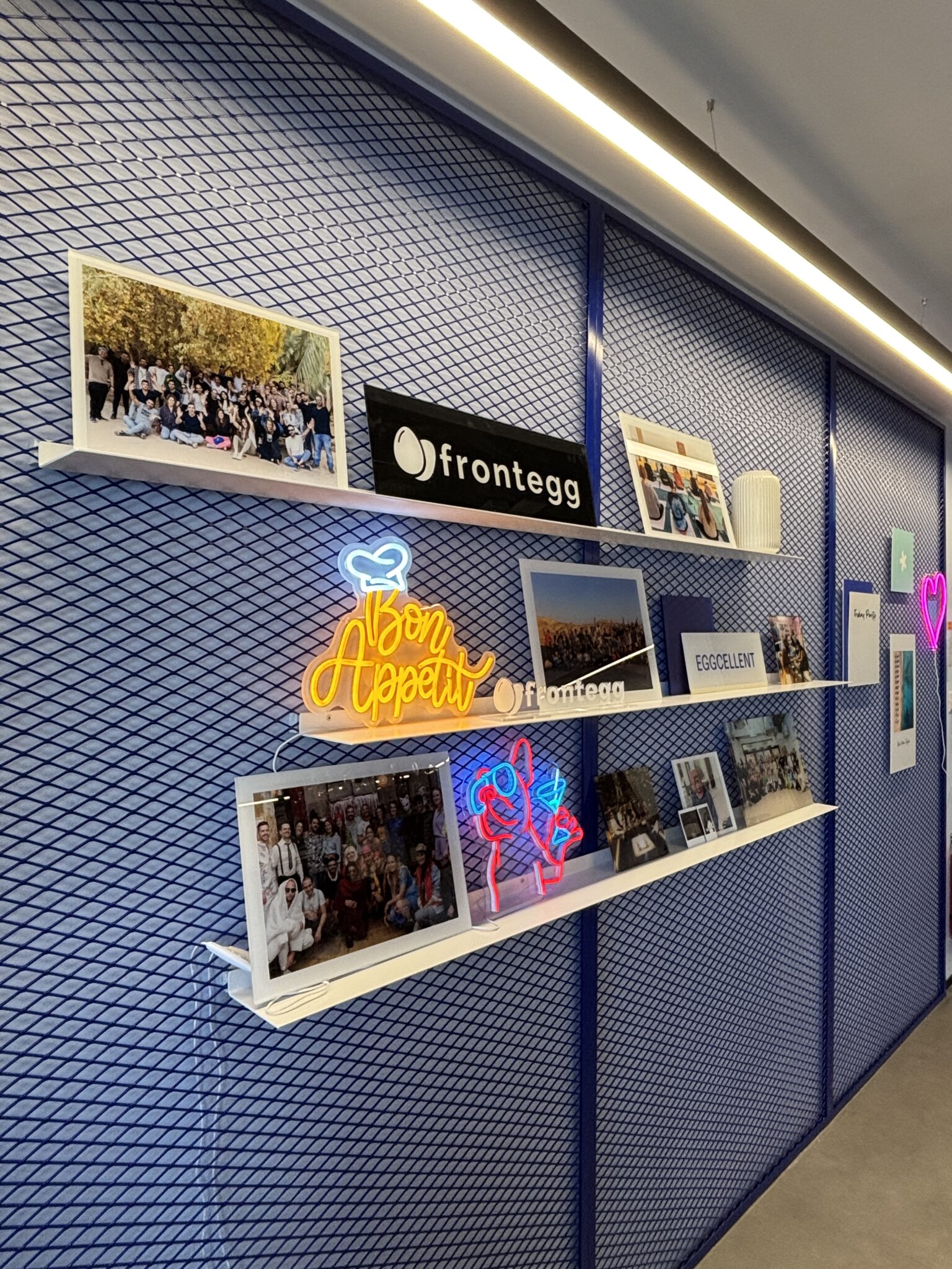 frontegg wall shelves with team photos and neon signs on blue mesh