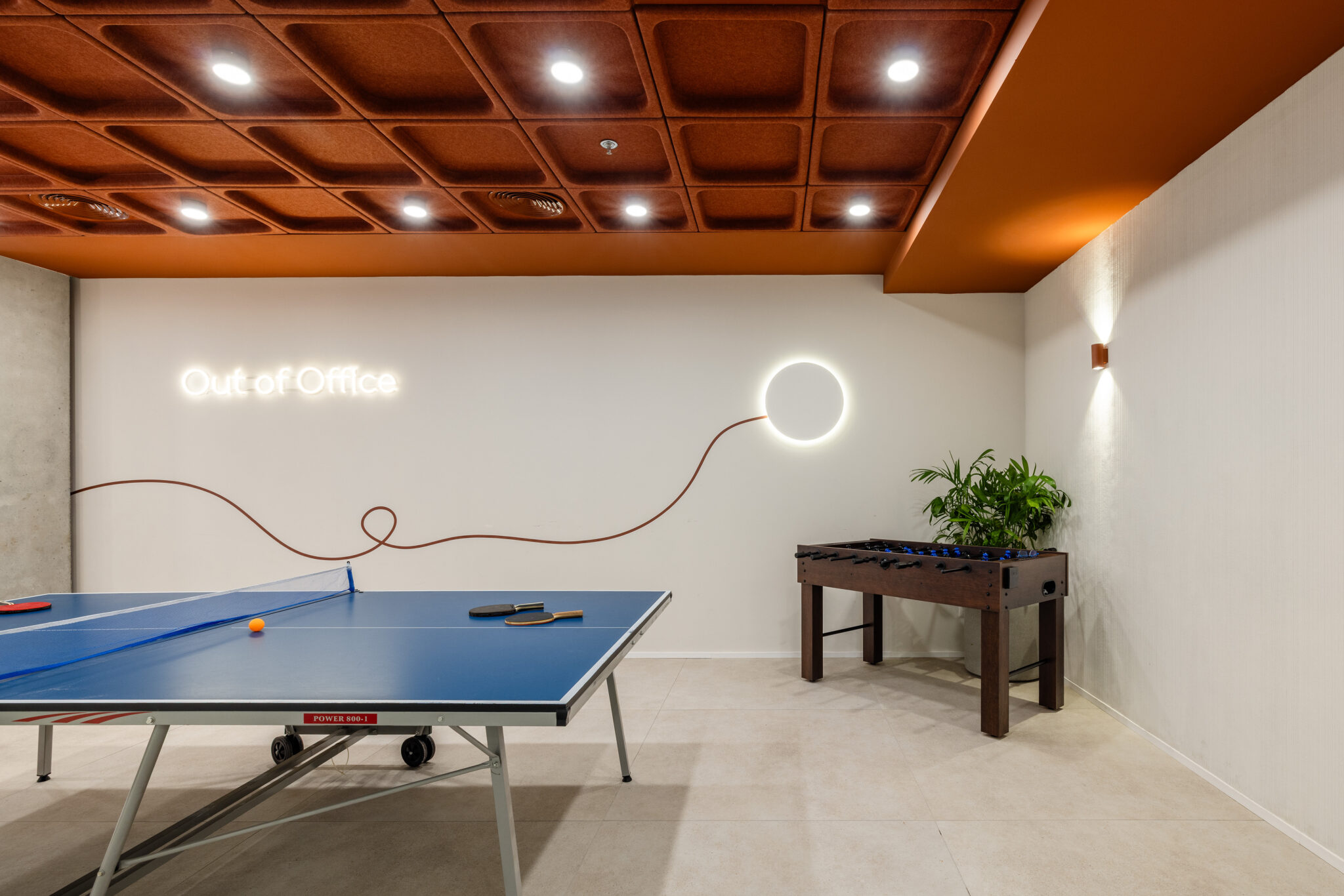 Ping pong table and foosball under an Out of Office neon sign