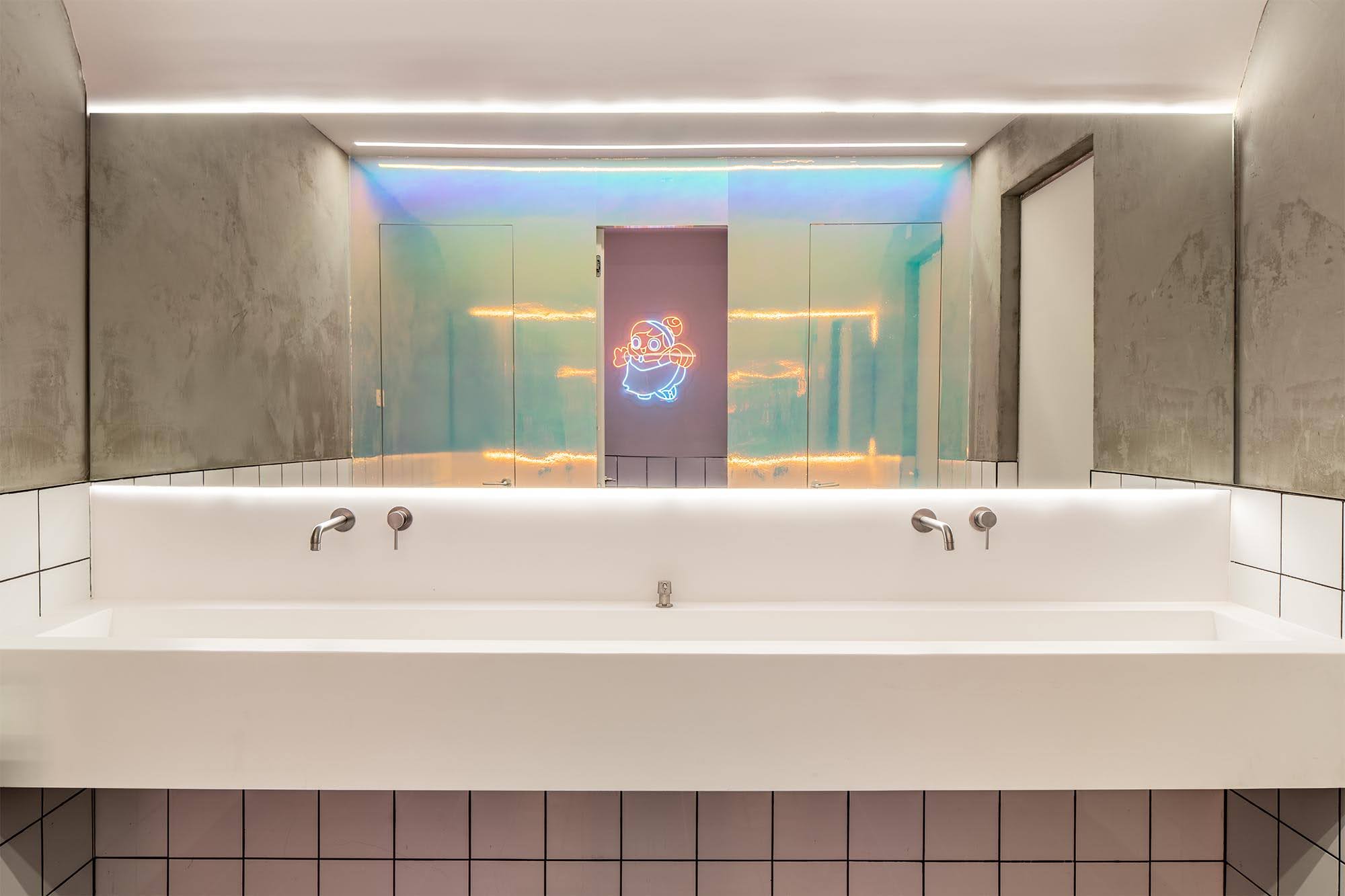 Long white washbasin with a neon character sign in the mirror